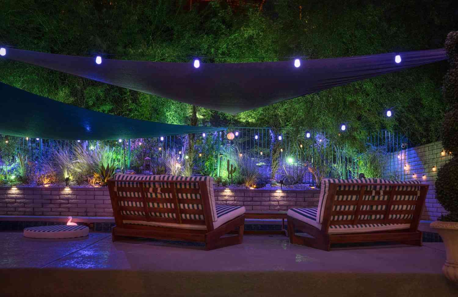 Outdoor patio with shade sails, lounge seating, and decorative landscape lighting in Long Island, NY